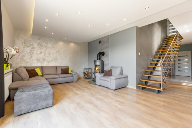 A modern living room with extra large sofa fireplace in industrial style, wood floor panels, textured wall finish, and wooden stairs